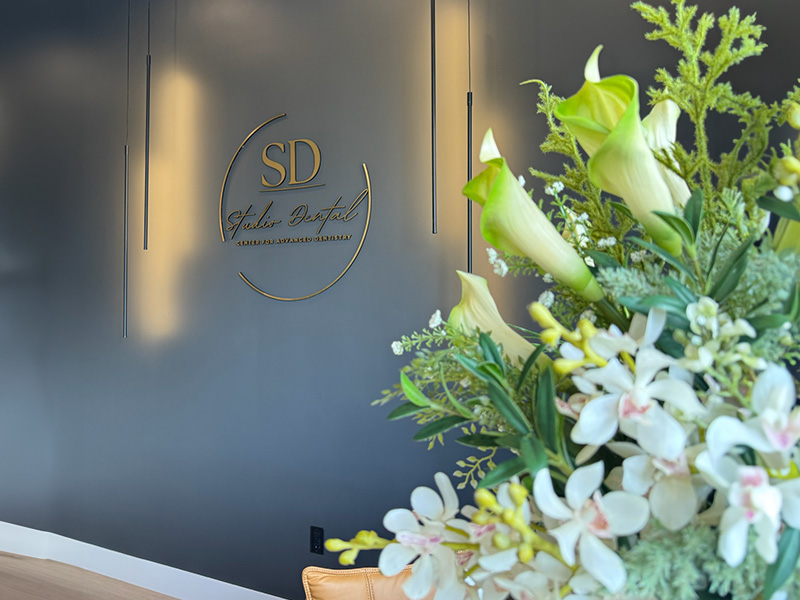 The image shows an interior space with a floral arrangement on a countertop, a sign with the text  SD  in a circular frame, and a wall-mounted light fixture.