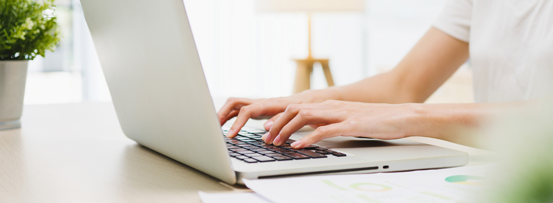 A person using a laptop computer at a desk with a blurred background.