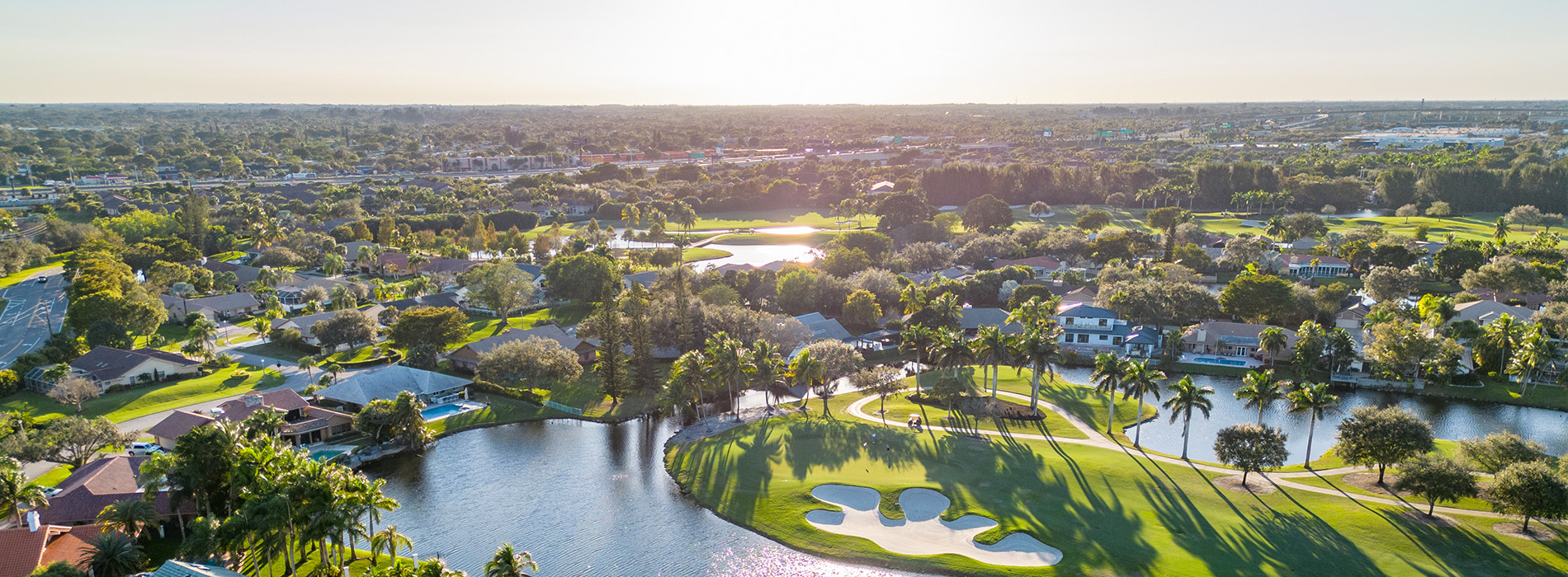 The image shows an aerial view of a residential area with a golf course during sunset, featuring clear skies and a colorful skyline.