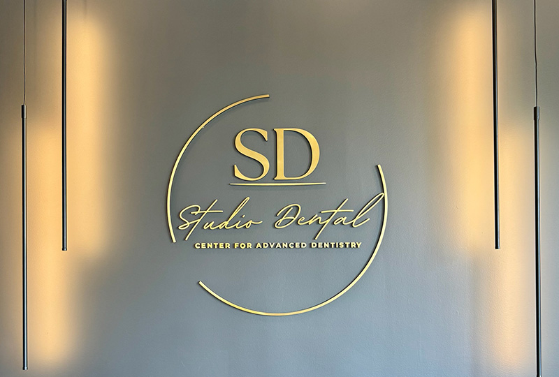 The image shows a sign with gold lettering on a silver background, featuring the logo of  SD Studio Dental  and the text  Center for Advanced Dentistry.