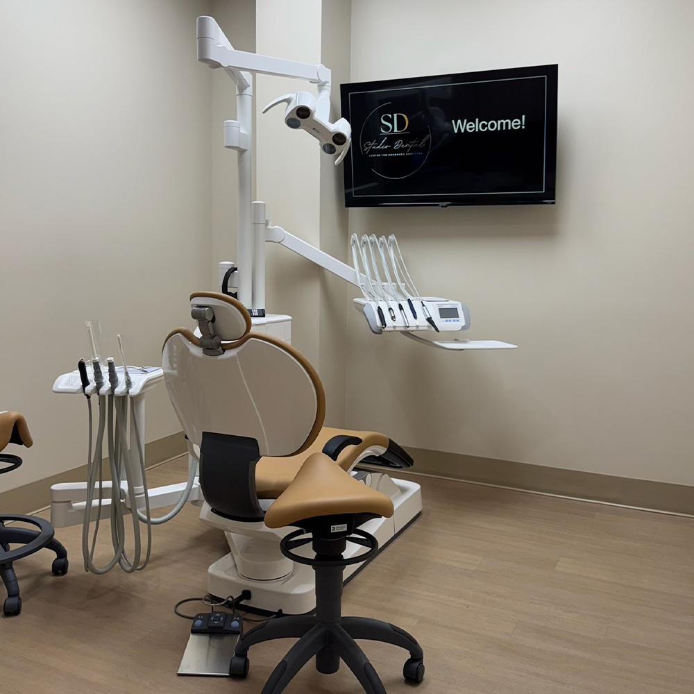 A dental office setting featuring a dental chair with adjustable equipment, a monitor displaying a  SD  logo, and a welcome sign on the wall.