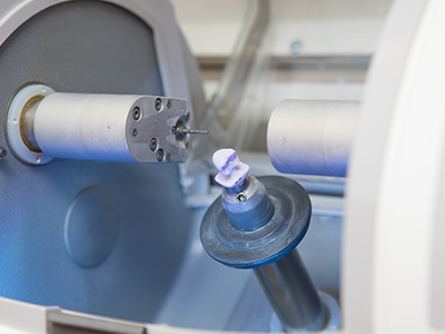 A large industrial machine with various mechanical components, including a visible spindle and an object being processed on a conveyor belt.
