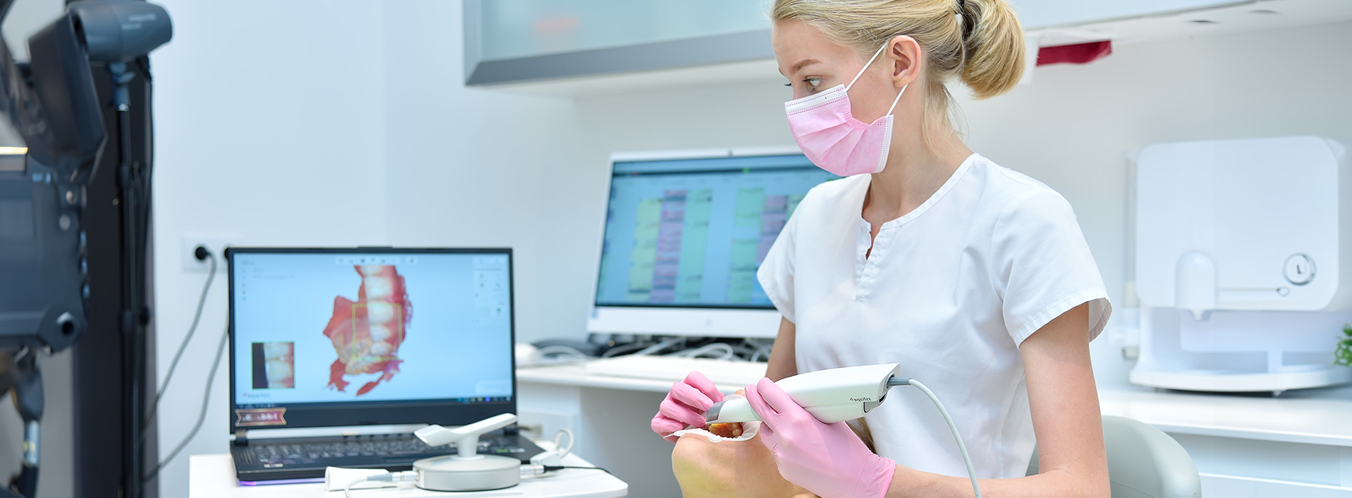 A woman wearing a white lab coat and pink gloves is using a microscope in a laboratory setting.