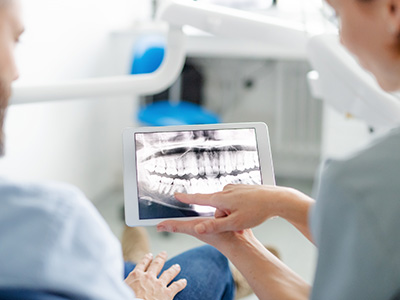 A dental professional showing a patient an X-ray on a tablet while seated in a dental chair.