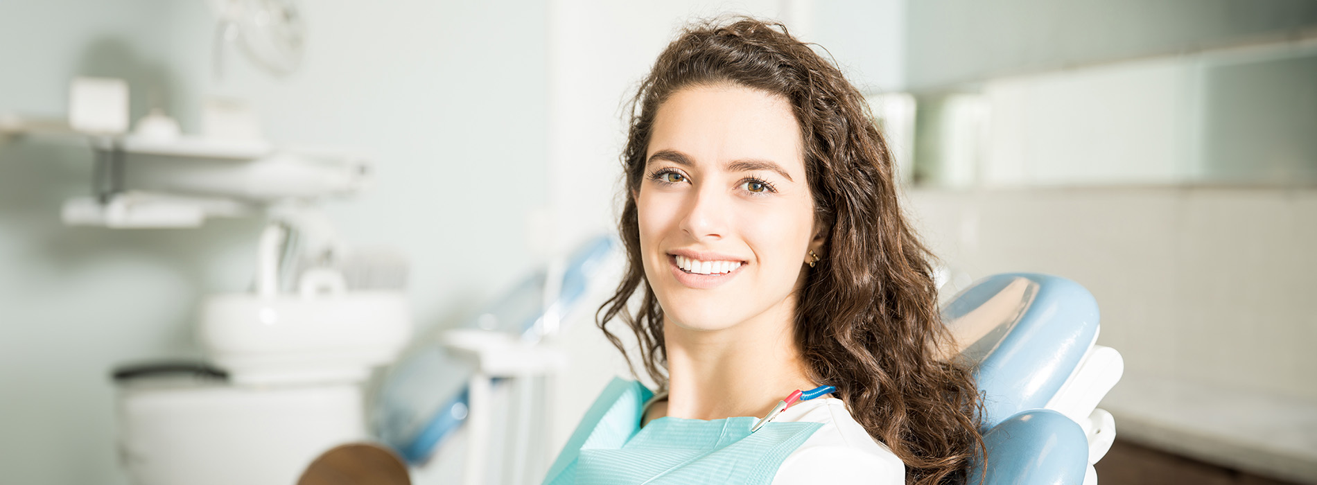 A woman with long brown hair smiling at the camera while seated in a dental chair.