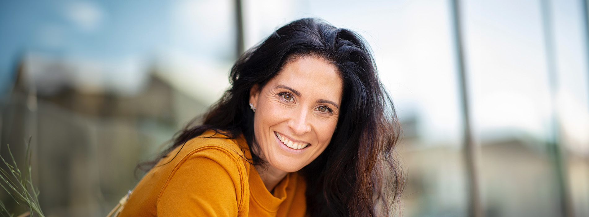 The image shows a woman with long hair smiling at the camera  she has light skin and appears to be indoors, wearing a yellow top.