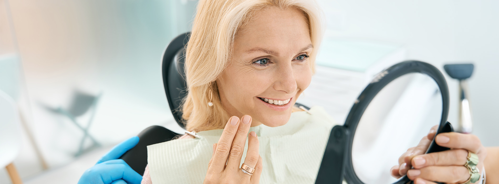 A woman sitting at a dental chair, smiling and looking towards the camera.