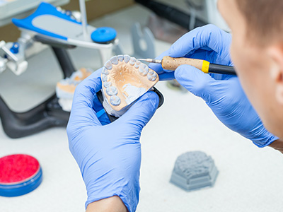 A person wearing gloves closely examines a tooth model with a magnifying glass.