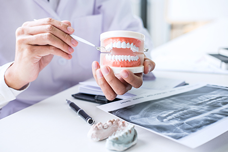 The image shows two photos side by side  on the left, a dental professional examines a patient s teeth with a tool  on the right, the same professional holds a cup containing a model of a human tooth and appears to be comparing it to a real tooth.