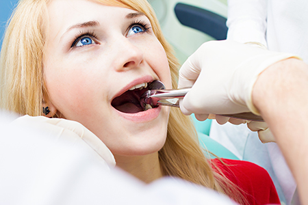 A young woman receiving dental care with a dentist performing an examination, surrounded by medical professionals in a professional setting.