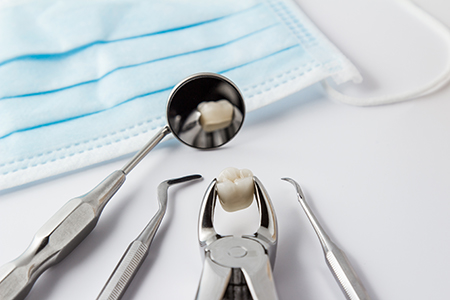 The image displays a collection of dental instruments, including a drill and a toothbrush with a small amount of toothpaste on its bristles, placed next to a blue surgical mask on a white surface.