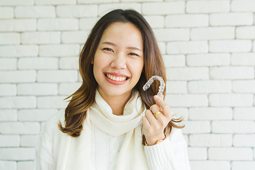 A woman holding a sign with a smiley face next to her mouth, wearing a white scarf and posing for the camera.