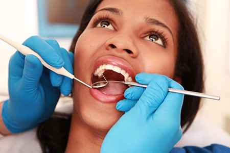 A person receiving dental care with a dental professional s hands visible, performing a procedure on their mouth while wearing blue gloves.