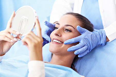 A woman sitting in a dentist s chair with her eyes closed while a dental professional holds up a magnifying glass over her face, examining her teeth.
