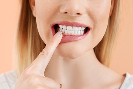 A woman with her finger on her teeth, appearing to be brushing them, set against a plain background.
