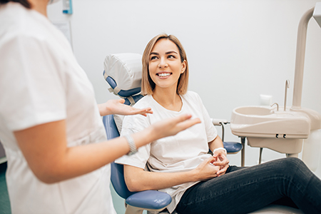 Woman in chair being attended to by dental professional, smiling at camera.
