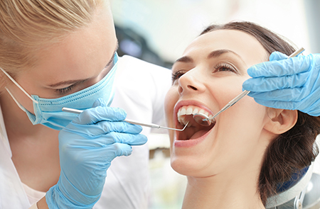 A woman receiving dental treatment while a dental hygienist works on her teeth with specialized tools.