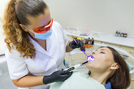 A dental hygienist is performing a teeth cleaning procedure on a patient while wearing personal protective equipment.
